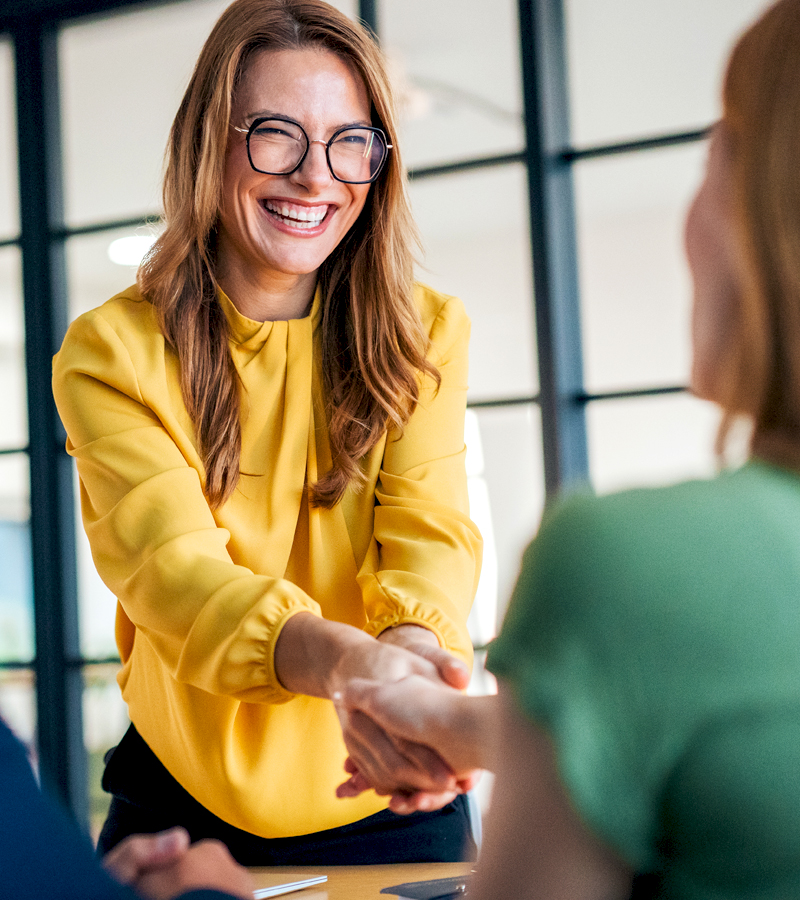 A white woman wearing glasses and shaking hands with businesswoman who just made a dream job offer