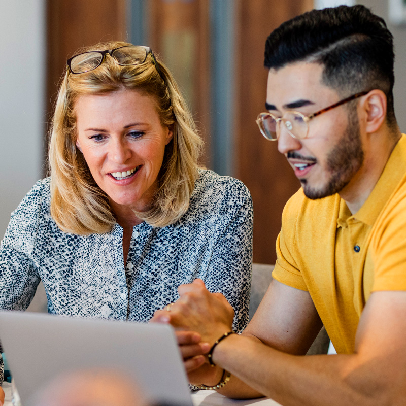 A blonde female mentor reviewing MCode results with her mentee, a young Asian man
