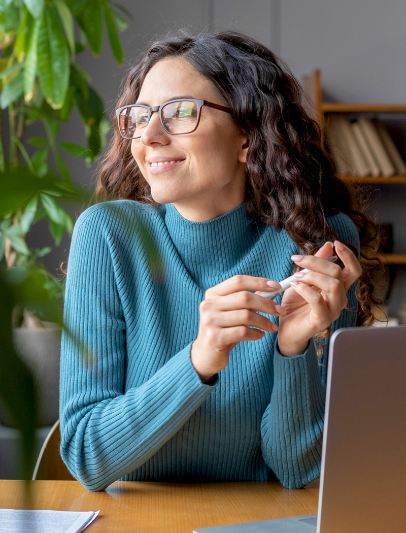 A young brunette woman wearing glasses and blue sweater who knows her Motivational Flow enjoying her work and experience increased job satisfaction
