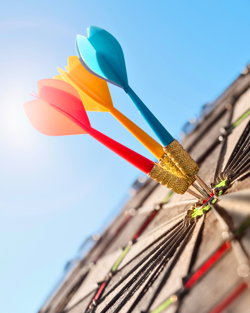 Three darts, red, yellow, and blue, all in the bullseye of a dart board to represent the impact of using motivation in sales pitches to close more deals