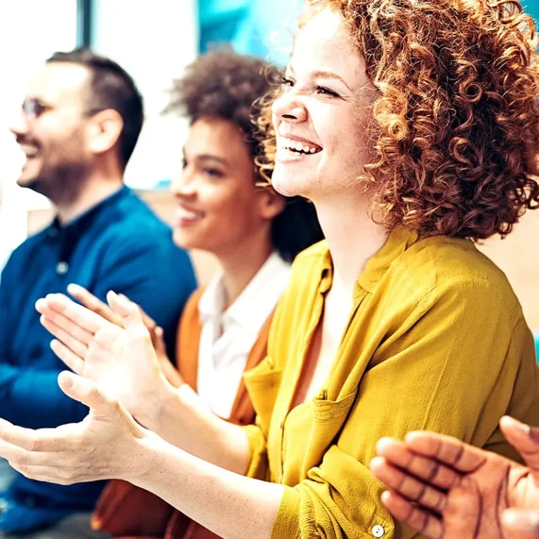 A woman with short curly red hair sitting among team members and clapping