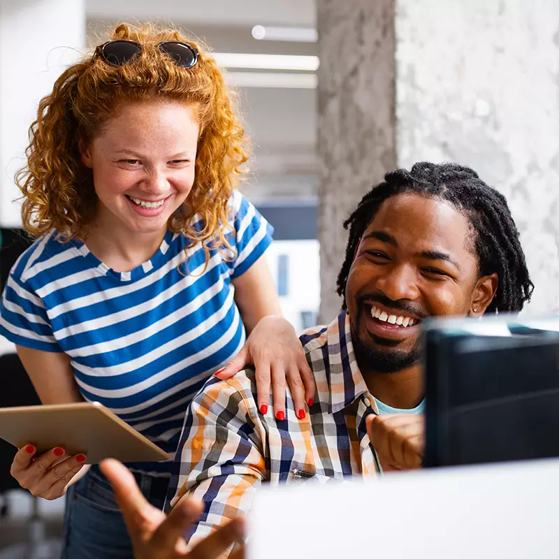 Two work colleagues laughing while looking at a website.